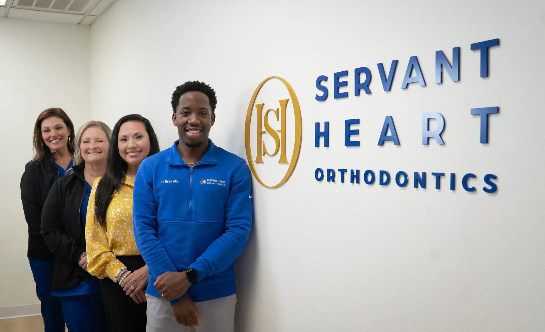 Servant Heart Orthodontics team standing beside the office sign in Rowlett, TX