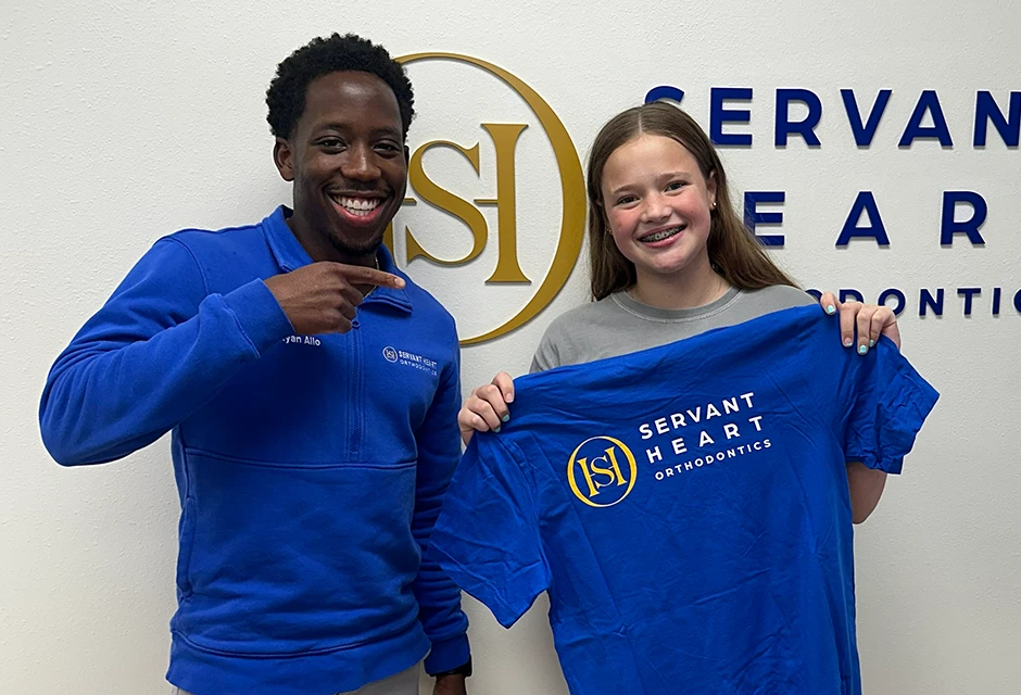 Teen patient holding a Servant Heart Orthodontics shirt beside Dr. Ryan Allo in Rowlett, TX